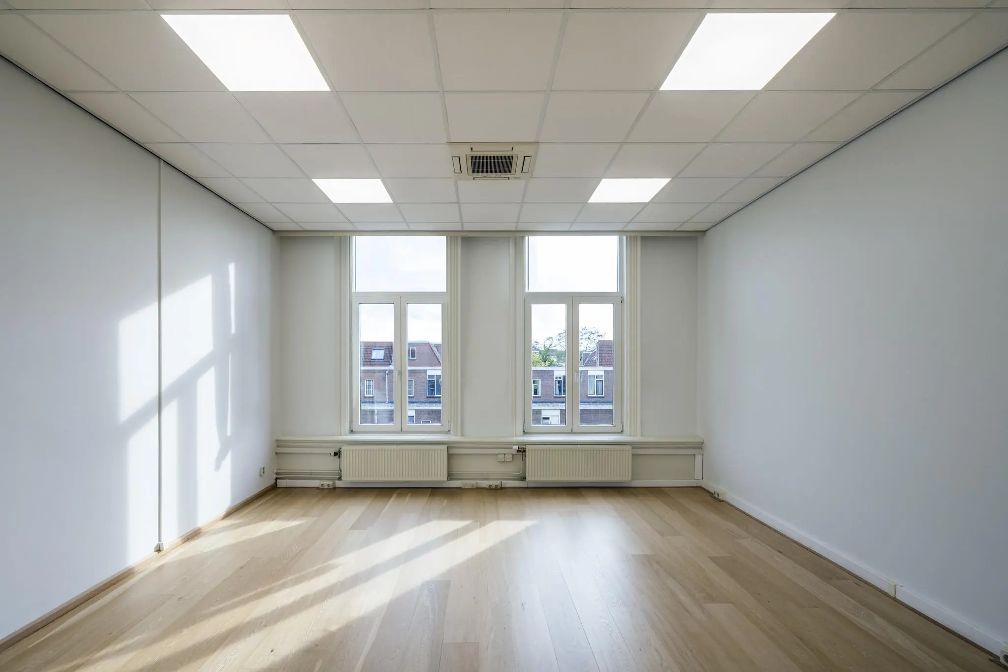 Licht en modern leeg kantoor met houten vloer en drie hoge ramen aan de Nieuwe Gracht.